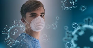 A young person wearing a face mask standing among graphic representations of the coronavirus.
