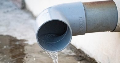 A drain pipe coming out of a wall, spilling water onto the ground.