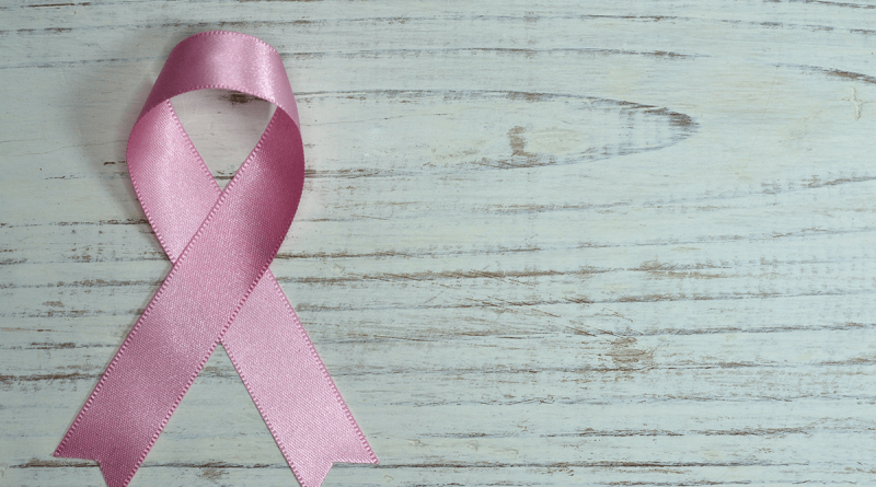 A pink breast cancer ribbon laying on a wooden table