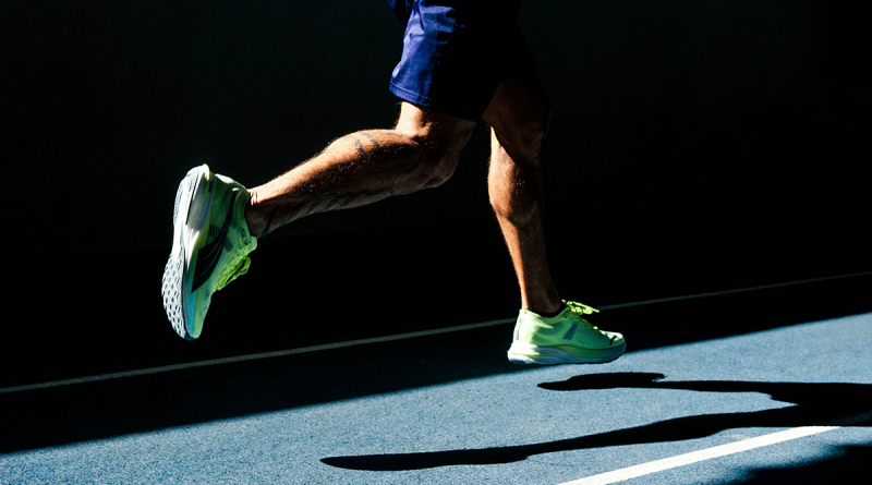 A person seen from behind, jogging on a dark track.