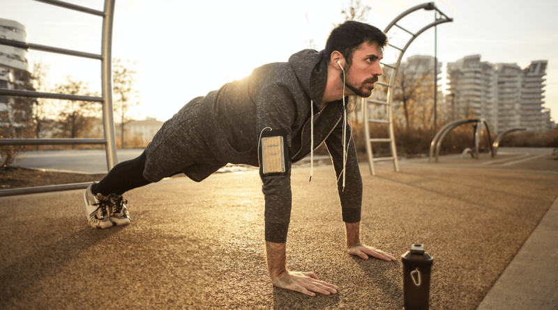 A person in the "up" position while doing pushups in a park with the sun rising behind them.