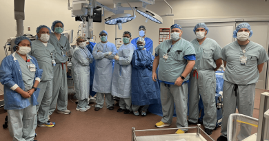 A large group of doctors wearing surgical scrubs posing in a surgery room.